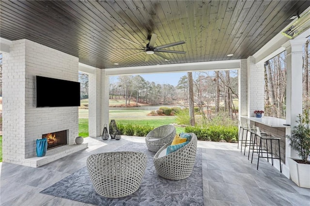 view of patio / terrace with outdoor dry bar, a ceiling fan, and an outdoor living space with a fireplace