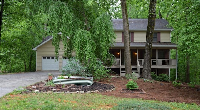 view of property hidden behind natural elements featuring an attached garage, driveway, and covered porch