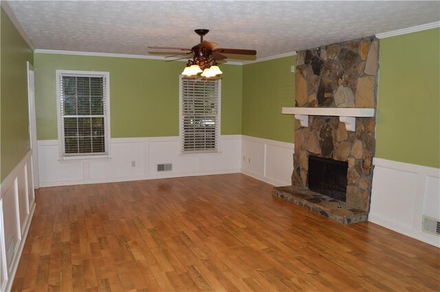 unfurnished living room with wainscoting, visible vents, wood finished floors, ceiling fan, and a stone fireplace