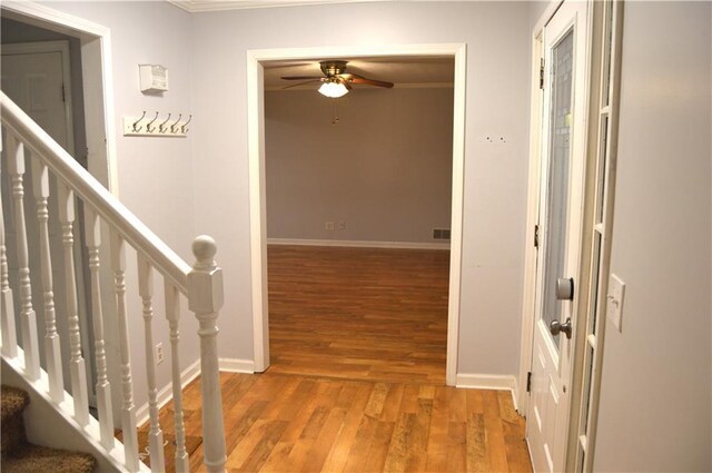 hall featuring light wood-type flooring, baseboards, visible vents, stairs, and ornamental molding