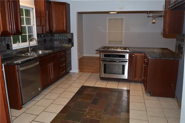 kitchen with a sink, dark stone counters, baseboards, decorative backsplash, and appliances with stainless steel finishes
