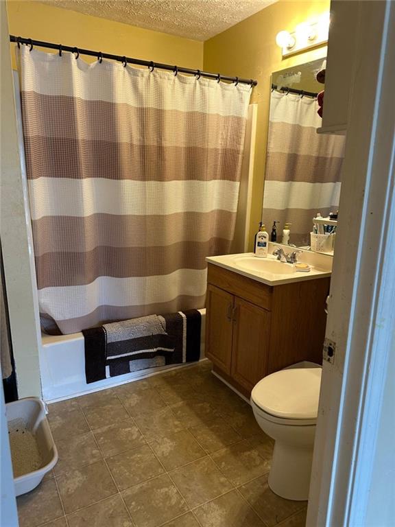 2195 Wilson Rd, Conyers, GA 30012 - bathroom featuring a textured ceiling, vanity, toilet, shower / bath combo, and tile patterned flooring