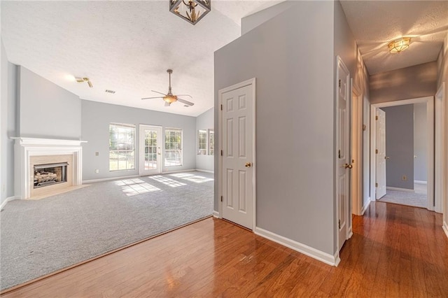 unfurnished living room with hardwood / wood-style floors, ceiling fan, a textured ceiling, and vaulted ceiling