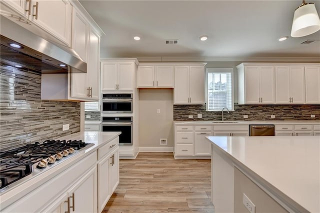 kitchen featuring sink, white cabinets, hanging light fixtures, stainless steel appliances, and light wood-type flooring