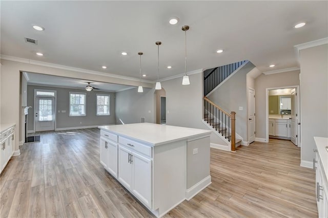 kitchen featuring crown molding, a center island, light hardwood / wood-style flooring, hanging light fixtures, and white cabinets