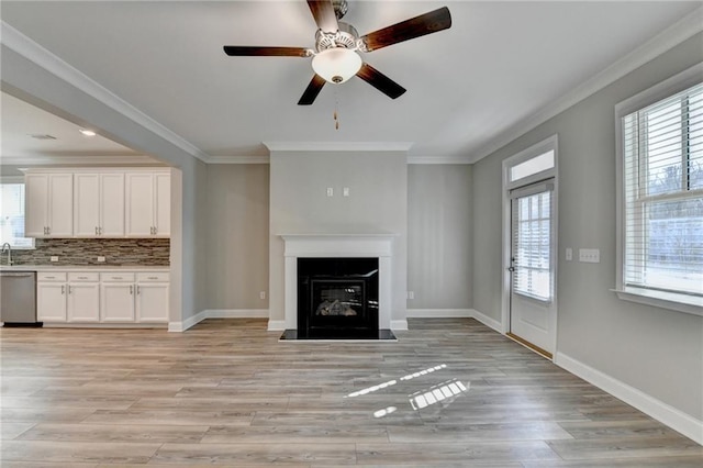 unfurnished living room featuring ornamental molding, plenty of natural light, sink, and light hardwood / wood-style floors