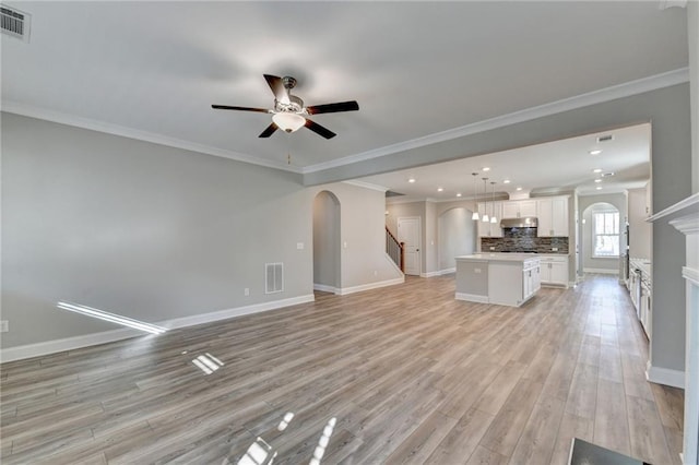 unfurnished living room with ceiling fan, ornamental molding, and light wood-type flooring