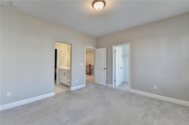 unfurnished bedroom with light carpet, a spacious closet, ensuite bath, and a closet