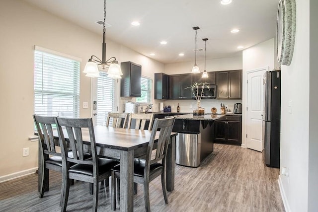 dining space with light hardwood / wood-style floors, plenty of natural light, and an inviting chandelier