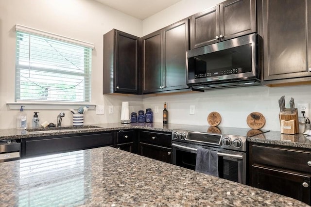 kitchen featuring dark brown cabinetry, stainless steel appliances, sink, and dark stone countertops