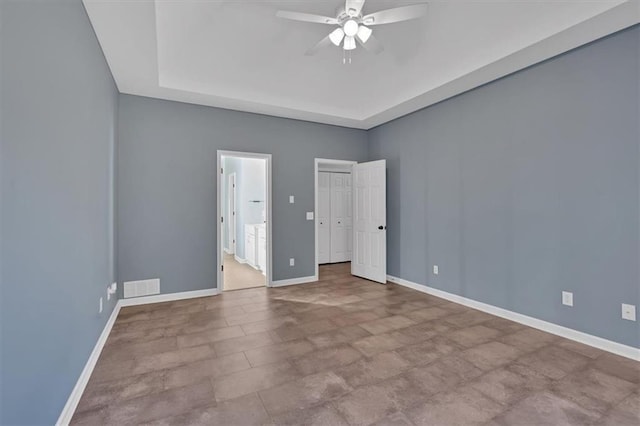 empty room with ceiling fan, a tray ceiling, visible vents, and baseboards