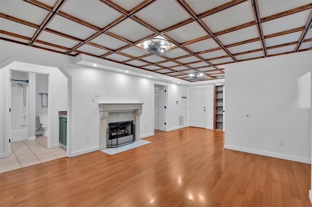 unfurnished living room with baseboards, a tiled fireplace, coffered ceiling, and light wood-style floors