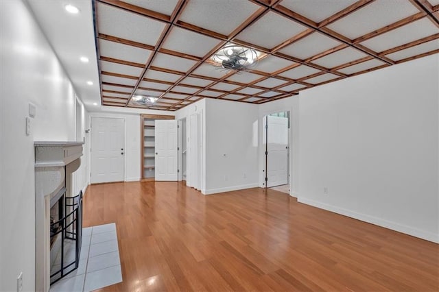 unfurnished living room featuring a fireplace with flush hearth, coffered ceiling, light wood-style flooring, and baseboards