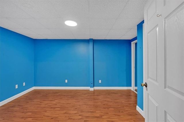 unfurnished room with wood finished floors, a paneled ceiling, and baseboards