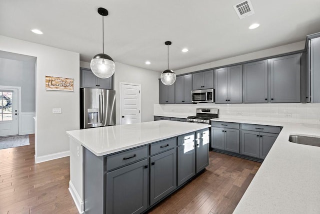 kitchen with appliances with stainless steel finishes, a kitchen island, dark wood finished floors, and gray cabinetry