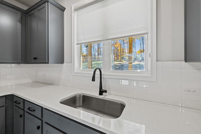 kitchen with tasteful backsplash, a sink, gray cabinetry, and light stone countertops