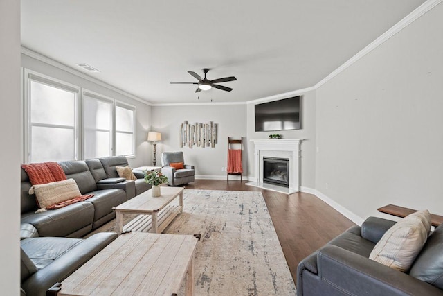 living area featuring visible vents, a glass covered fireplace, wood finished floors, and ornamental molding