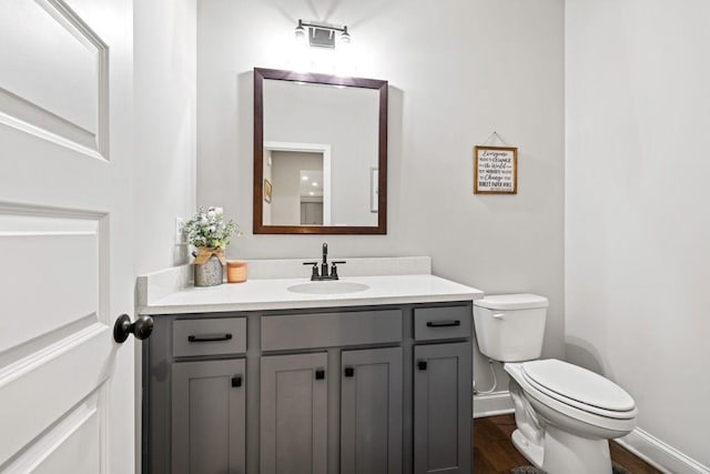 half bath featuring wood finished floors, vanity, toilet, and baseboards