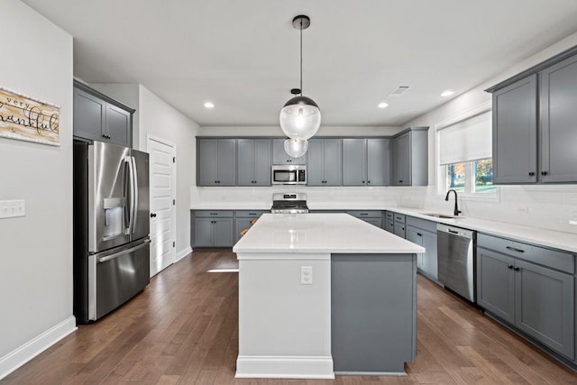 kitchen featuring dark wood finished floors, gray cabinets, appliances with stainless steel finishes, a sink, and a kitchen island