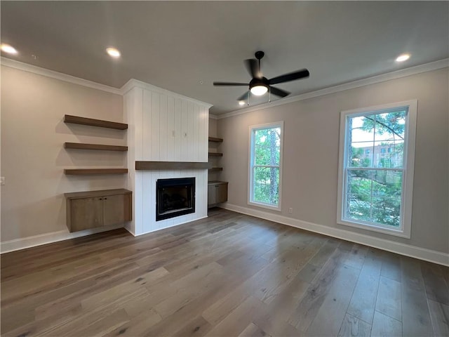 unfurnished living room with ornamental molding, a large fireplace, ceiling fan, and dark hardwood / wood-style flooring