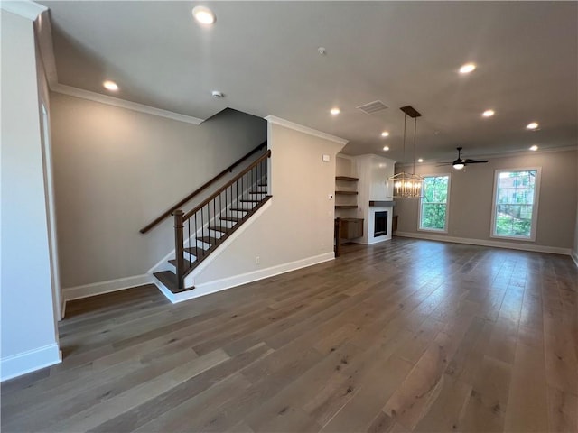 unfurnished living room featuring ceiling fan with notable chandelier, dark wood-type flooring, and ornamental molding