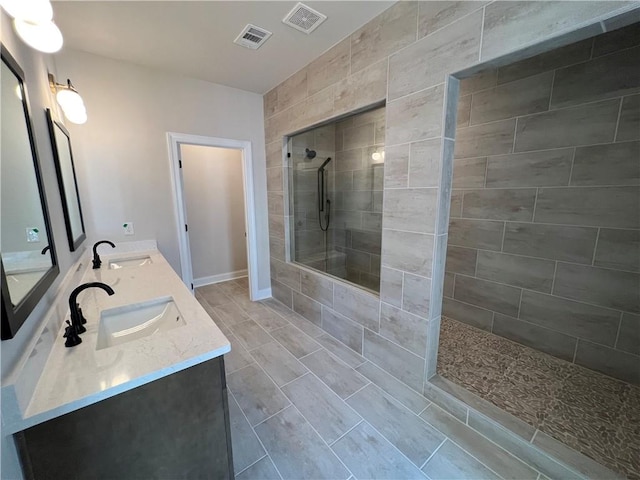 bathroom with large vanity, tiled shower, dual sinks, and tile flooring