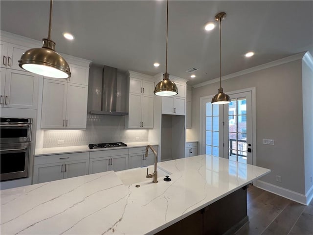 kitchen with decorative light fixtures, wall chimney range hood, crown molding, backsplash, and sink