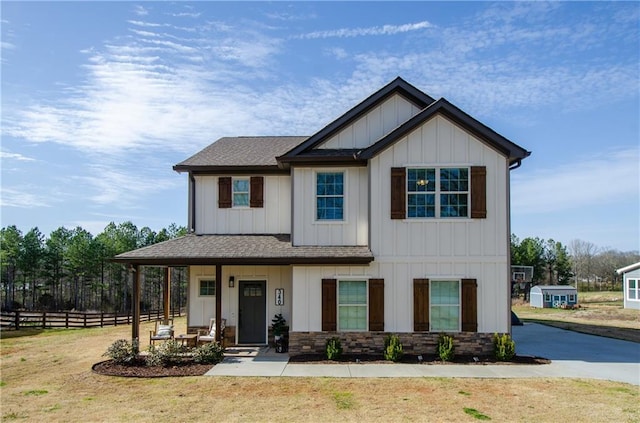 view of front of house with a front lawn, fence, covered porch, board and batten siding, and a shingled roof