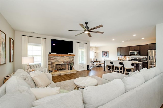 living area with wood finished floors, visible vents, a fireplace, recessed lighting, and ceiling fan with notable chandelier