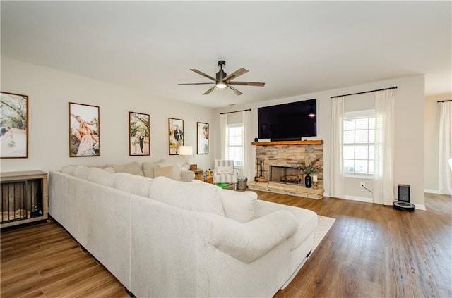 living room featuring a stone fireplace, baseboards, a ceiling fan, and wood finished floors