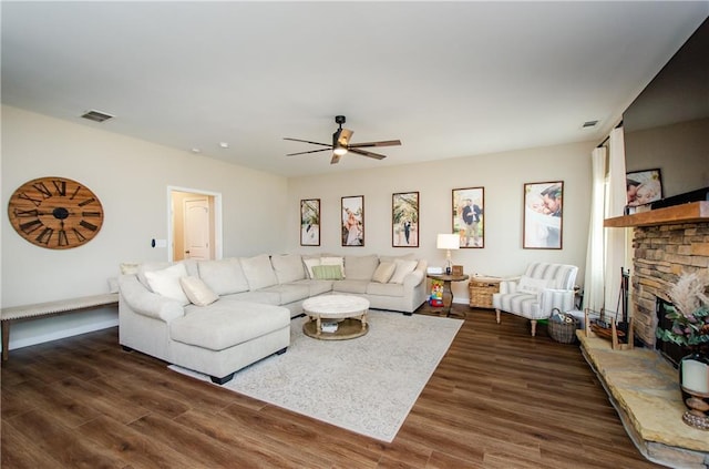 living room with visible vents, a ceiling fan, a stone fireplace, and dark wood-style flooring