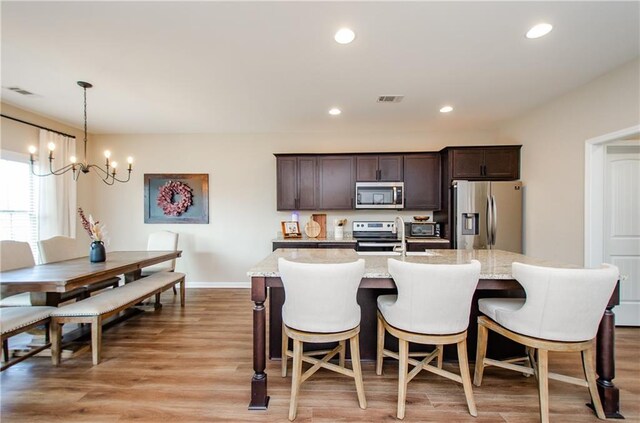 kitchen with visible vents, a kitchen island with sink, dark brown cabinets, light wood-style floors, and appliances with stainless steel finishes