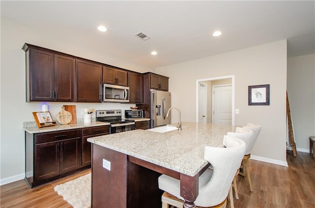 kitchen featuring visible vents, a kitchen island with sink, dark brown cabinets, appliances with stainless steel finishes, and a kitchen breakfast bar