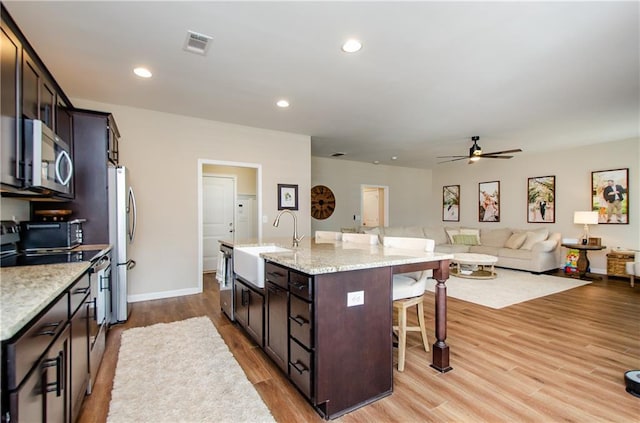 kitchen with visible vents, a breakfast bar, a center island with sink, light wood-style floors, and appliances with stainless steel finishes