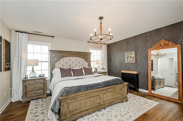 bedroom with visible vents, an accent wall, baseboards, dark wood finished floors, and an inviting chandelier