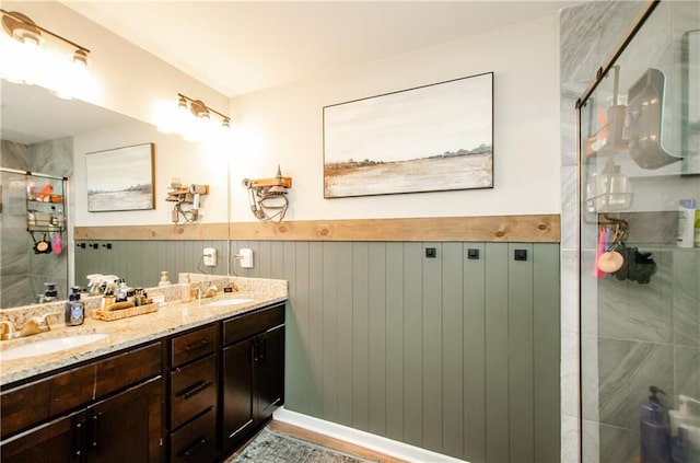 full bath with double vanity, wainscoting, a stall shower, and a sink