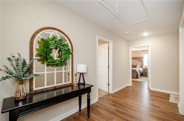 hallway featuring attic access, wood finished floors, and baseboards