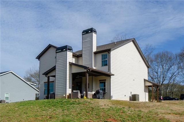 rear view of property with central AC unit, a lawn, and a chimney