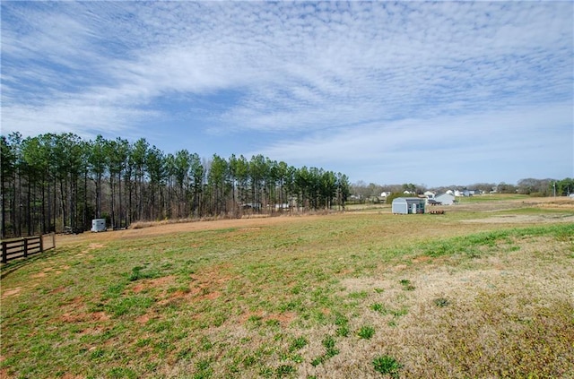 view of yard featuring a storage shed, an outbuilding, fence, and a rural view