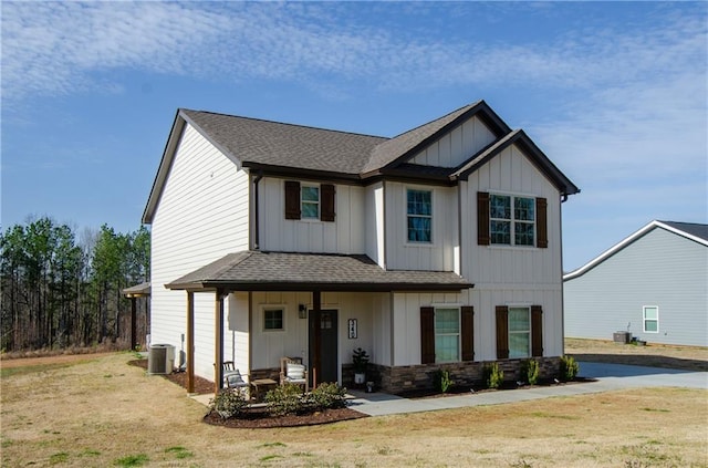 view of front facade with central AC unit, board and batten siding, a shingled roof, and a front yard