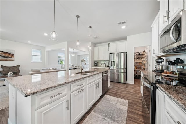 kitchen with a sink, an island with sink, stainless steel appliances, open floor plan, and dark wood-type flooring