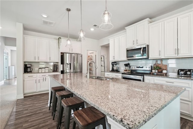 kitchen with visible vents, decorative backsplash, a center island with sink, a sink, and appliances with stainless steel finishes