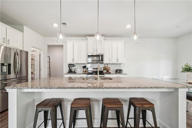 kitchen featuring a breakfast bar area, appliances with stainless steel finishes, a sink, white cabinets, and an island with sink