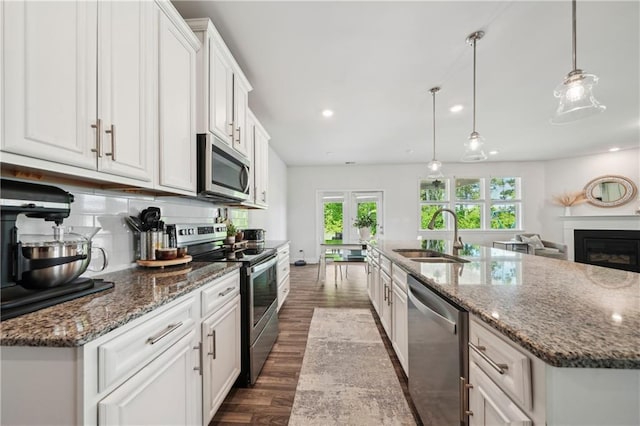 kitchen featuring a kitchen island with sink, dark wood finished floors, a sink, stainless steel appliances, and white cabinetry