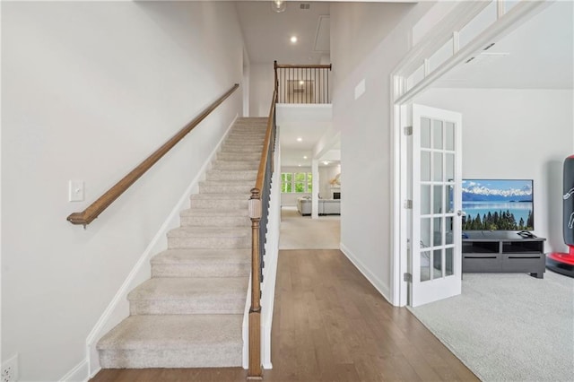 stairs featuring recessed lighting, baseboards, wood finished floors, and a towering ceiling