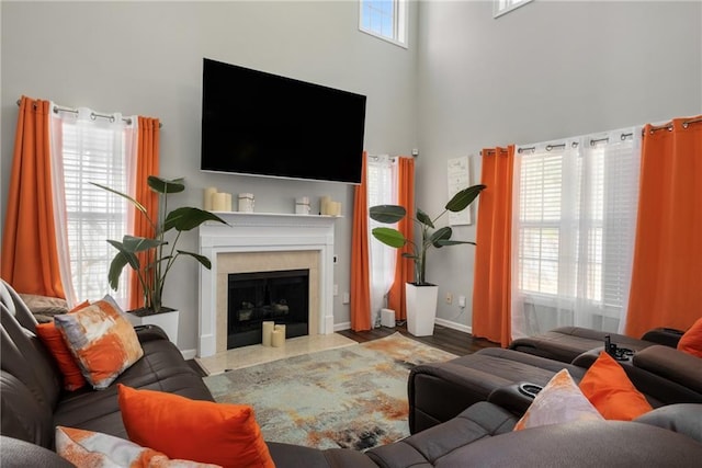 living area featuring a high ceiling, a fireplace with flush hearth, a healthy amount of sunlight, and baseboards