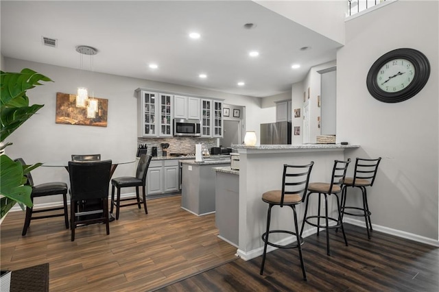 kitchen with visible vents, dark wood-type flooring, a breakfast bar area, appliances with stainless steel finishes, and a peninsula