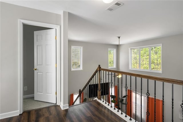 hallway featuring wood finished floors, an upstairs landing, visible vents, and baseboards