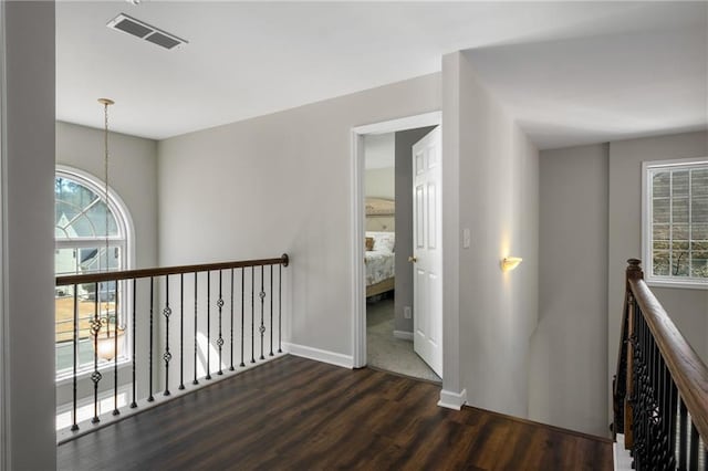 corridor with dark wood-type flooring, an upstairs landing, visible vents, and baseboards