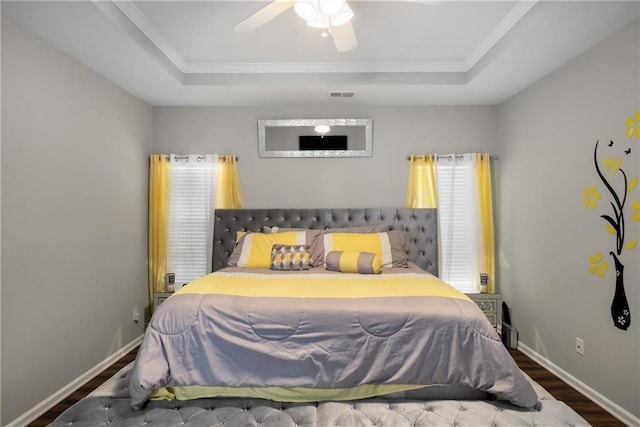 bedroom with visible vents, a raised ceiling, baseboards, and wood finished floors